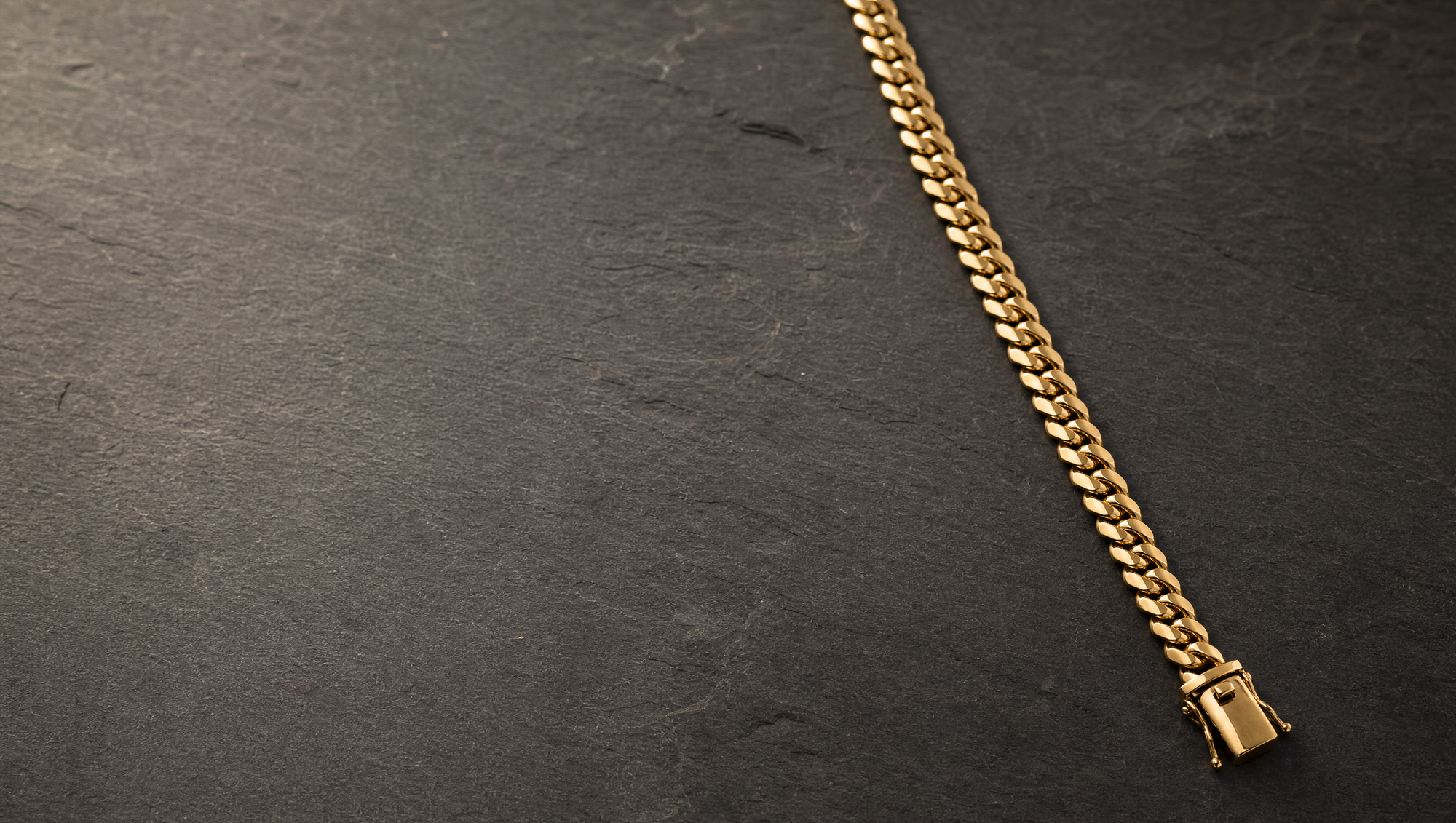 A heavy gold cuban link chain laid open in a long diagonal across dark slate