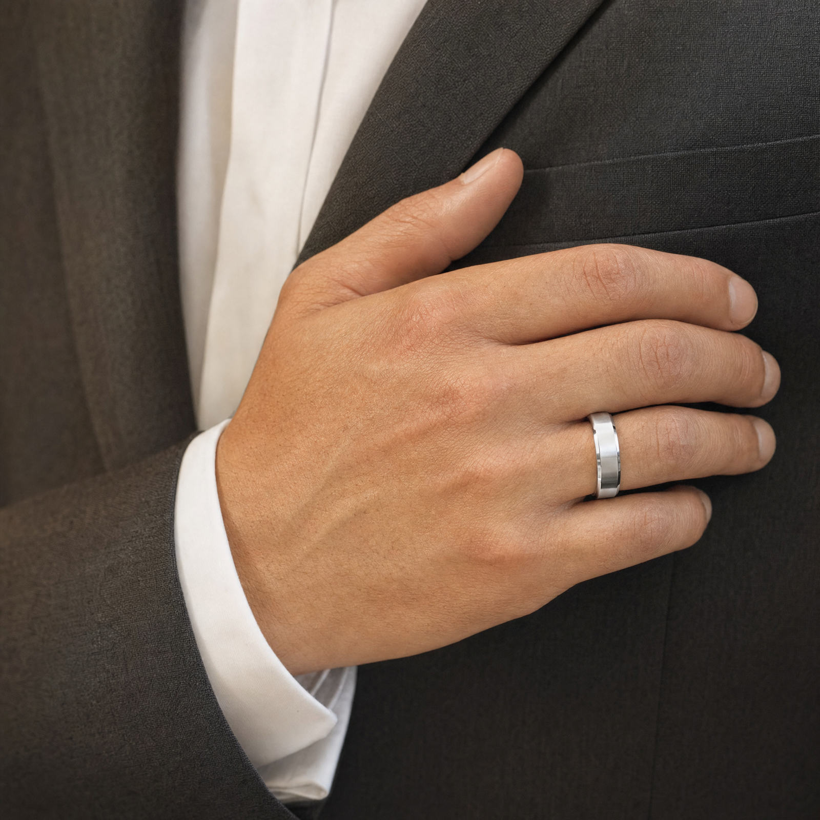 Silver — beveled silver band on the ring finger against a charcoal suit